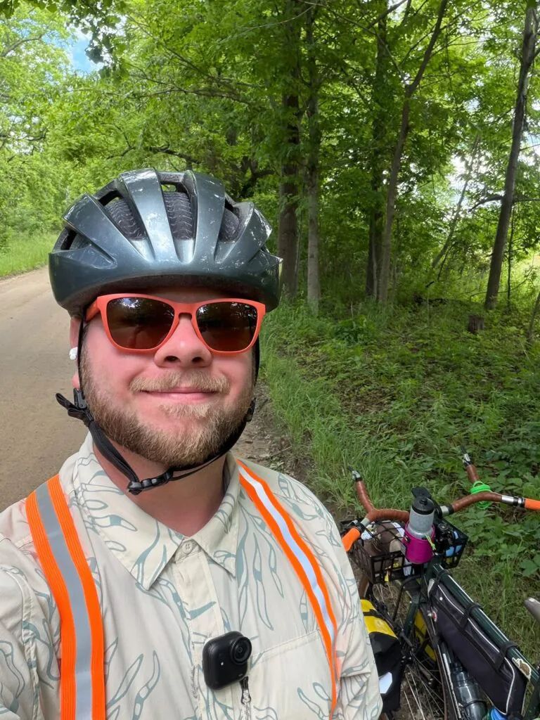 Trevor Sullivan wearing a biking helmet and GoPro-style camera in the woods with his bike.