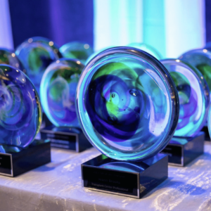 Many blue and green, rounded glass awards with black pedestals sit on a table waiting to be presented.